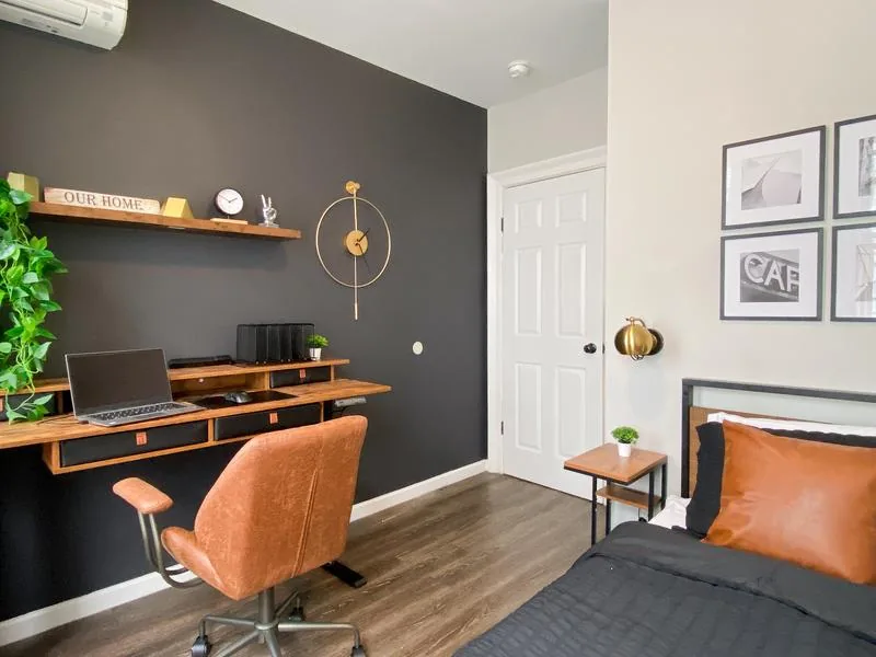 Bedroom 1 — charcoal accent wall, work desk with cognac chair, brass clock